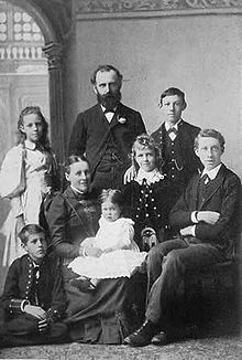 photographie noir et blanc : portrait de famille, un homme barbu debout au centre, sa femme assise devant lui avec trois filles et trois garçons