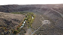 Drone image of the West Little Owyhee River at Anderson crossing. This image is from September, so the water is very low. Lush green plants flank the river for 10-20 feet on each side, then becomes sagebrush.