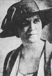 White woman with dark eyes, wearing a wide-brimmed hat.