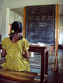 A girl in Bangladesh sitting at a desk in front of a blackboard