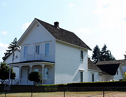 Photograph of the Caples house, a two-story, whitewashed farmhouse with outbuildings behind