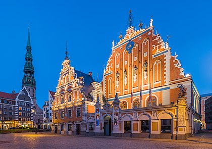 Casa dos Cabeças Pretas e a torre da igreja de São Pedro, Centro Histórico de Riga, Letônia. A Irmandade dos Cabeças Pretas é uma associação de mercadores locais do sexo masculino, proprietários de navios e estrangeiros que atuava na Livônia (atual Estônia e Letônia) em meados do século XIV até 1940, mas ainda permanece ativa na atual Hamburgo. A Irmandade dos Cabeças Pretas foi fundada como uma organização militar, mas os aspectos não militares da associação tornaram-se gradualmente mais pronunciados até que a Irmandade se tornou uma organização predominantemente social após o fim da Grande Guerra do Norte. A origem exata do termo “Cabeças Pretas” é desconhecida. O santo padroeiro da Irmandade é o negro egípcio cristão São Maurício, cuja cabeça também está representada no brasão da Irmandade. Se o santo padroeiro foi escolhido por causa do nome, ou se o santo precede o nome permanece obscuro. (definição 7 000 × 4 922)