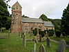 Stone building with
                            square tower. In the foreground are
                            gravestones.