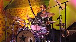 A colour photograph of Starr playing a dark coloured drum kit on a stage. The background is yellow.