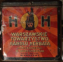 Une boîte rouge en métal sur laquelle est écrit "Warszawskie Towarzystwo Handlu Herbatą"