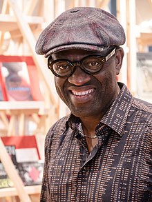 Photo noir et blanc d'un homme souriant, noir, avec casquette et lunettes