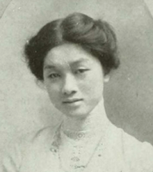 A young Chinese woman, her dark hair parted and center and dressed in an updo, wearing a high-collared white blouse