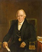 Man seated, wearing a dark suit and a chain of office