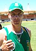 A white coloured man wearing a green cap and t-shirt and giving a thumbs-up.