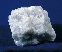 An irregularly shaped rock, milky-white in color. The rock glistens or sparkles from the overhead lights.
