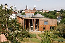 Ein Holzgebäude mit der Aufschrift NAWAREUM. Rundherum ist ein Garten. Im Hintergrund sieht man die Stadt Straubing mit ihren charakteristischen Türmen.