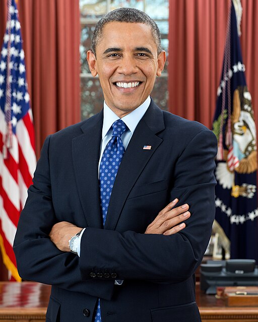Obama standing with his arms folded in addition to smiling.
