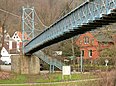 Das Foto zeigt eine hellblau angestrichene Hängebrücke, die aufwändig aus Metallgitterwerk erbaut wurde.