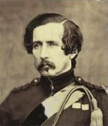 Black and white photographic portrait of a white man with dark hair and moustache in military uniform