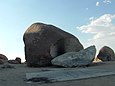 30 m hoher, rundlicher Felsbrocken in der Wüste, davor ein großes Bruchstück mit Graffiti