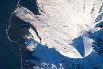 Спутниковый снимок заснеженной вулканической вершины с ледником, впадающим прямо в океан.