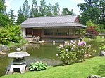 Het Japans ceremoniehuis is opgetrokken uit natuurlijke materialen. Op de voorgrond een steenlantaarn.