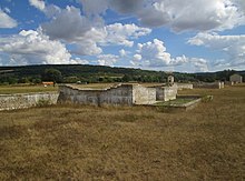 Présentation d'édifices en ruines adossé à un mur.