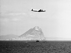 Plane flying over a submarine, with the Rock of Gibraltar in the background