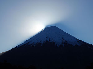 Sun setting behind the peak, highlighting the drifting snow.