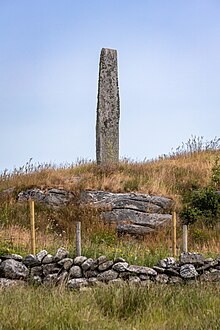 Senkrechter Bautastein auf grünem Hügel