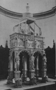 Black and white photograph of a stone structure comprising, from bottom to top, caryatids, a sarcophagus with sculpted walls, a recumbent and a statue.