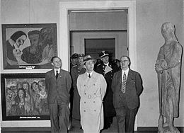 photo en noir et blanc montrant Goebbels entouré de quatre hommes entrant dans une salle d'exposition, avec une statue à droite et deux tableaux à gauche