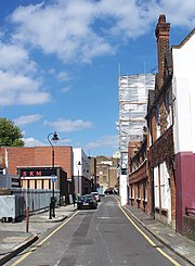 A long narrow deserted street. On the right of the picture a long row of traditional English red brick cottages line the street, while the left side of the street is lined with modern industrial units.