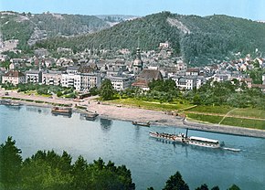 Kolorovaná pohlednice, foto z levého břehu Labe směrem na pravý břeh, v popředí Labe s přístavem, uprostřed kostel s farou, zleva i zprava obklopeny městskou zástavbou, v pozadí zalesněné kopce