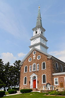 A brick church surmounted by a white tower, then a short grey steeple