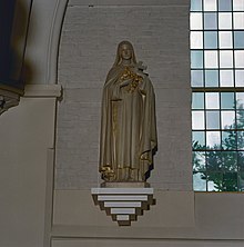 Stone or plaster statue of a woman in long robes, edged in gold, holding a crucifix