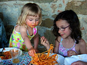 Two young girls sharing a plate of spaghetti. ...