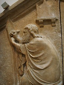 A relief against a wall shows a bearded man reaching up with his hands as his clothes are draped over his body.
