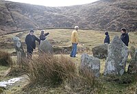Five warmly-dressed people looking at a stone circle