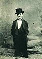 Little Tich on stage in costume while singing "I Could Do—Could Do—Could Do With a Bit" in the 1890s