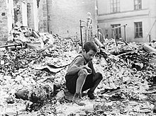 Photo noir et blanc prise en septembre 1939, à Varsovie. Au centre de la photo, un enfant se tient accroupi dans les gravats d’un bâtiment en ruine.