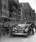 Hitler hilser med utstrakt arm paraderende SA-menn under rikspartidagene i Nürnberg i november 1935. Bak i bilen står «Blodsfanen», partiets seremonielle hakekorsflagg.