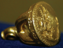 A small golden stamp seal, shaped like a bell, with cuneiform inscriptions and the image of a woman standing before a goddess.
