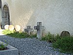 Kreuze und scheibenförmige Grabstelen an der Wand der Pfarrkirche