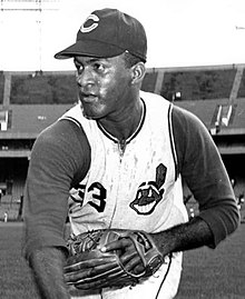 A man in a light baseball uniform and dark undersleeves cap