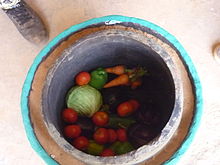 A clay pot with another clay pot inside and wet sand between the two; the inner pot has vegetables in it