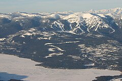 Вид с воздуха на лесной горный район с лыжными трассами. На переднем плане частично замерзший водоем.