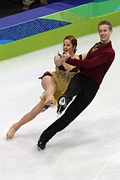 Samuelson und Bates auf der Eisfläche während ihres Kürtanzes. Bates trägt ein weinrotes Hemd zu einer schwarzen Hose, Samuelson ein gold-gelbes Kleid. Im Hintergrund ist die Bande im dunkelblau-hellgrünen Design der Vancouver-Spiele 2010 zu sehen.