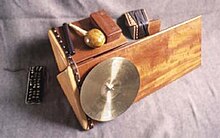 Photograph of an unconventional music instrument made of wood with a cymbal attached to the side