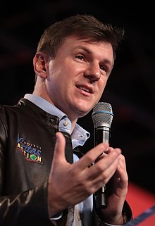 O'Keefe speaking into a microphone and gesturing with his right hand