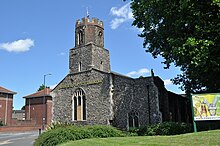 View of the church bathed in bright sunlight. There is a 3-stage tower at the near end.