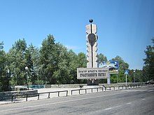 Monument en forme de stèle/obélisque photographié depuis un véhicule circulant sur la route.