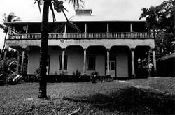 Photograph of a two-story building with broad verandas in a tropical setting
