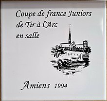 Photo d'un carreau de faïence avec un dessin au trait de la cathédrale d'Amiens, avec l'inscription coupe de France juniors de tir à l'arc en salle, Amiens 1994.