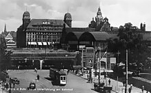 Sepia-tone picture postcard with Victorian-era building with wagons, people and train cars out front; original caption in German: "Essen und Ruhr Neue Unterfuhring am Bahnhof" (?)